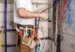 Electrician holding electrical wires during house wiring work with tool belt and tools